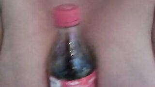 Naked girl holds a coke bottle between her boobs