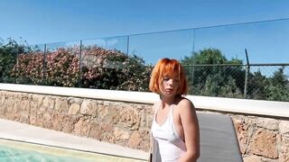 Charming red-haired girl sunbathing by the pool in a sexy swimsuit