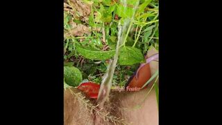 Village woman in a red tunic is pissing in the middle of a green field