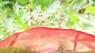 Village woman in a red tunic is pissing in the middle of a green field